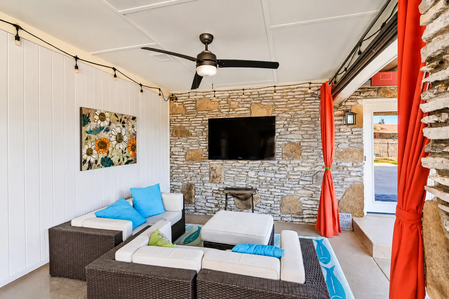Covered outdoor lounge with string lights and stone wall